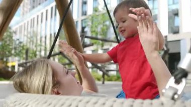 Anne, küçük oğluyla yürüyüş yaparken eğleniyor. Genç anne, bebeğiyle salıncakta sallanıyor.