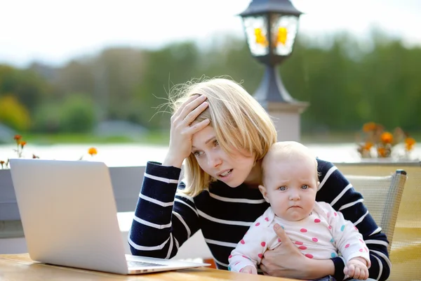 Cansada joven madre trabajando oh su portátil — Foto de Stock