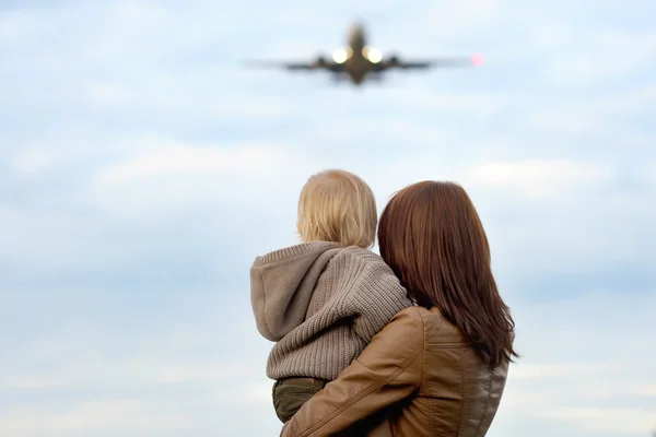 Mujer sosteniendo niño pequeño con avión en el fondo — Foto de Stock