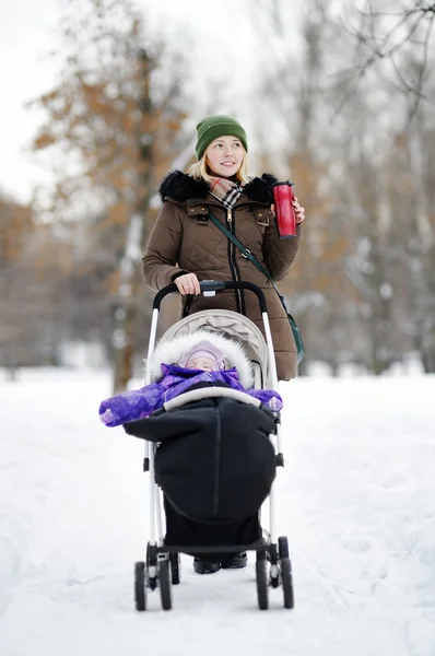 Madre joven caminando con el bebé en el cochecito en invierno — Foto de Stock