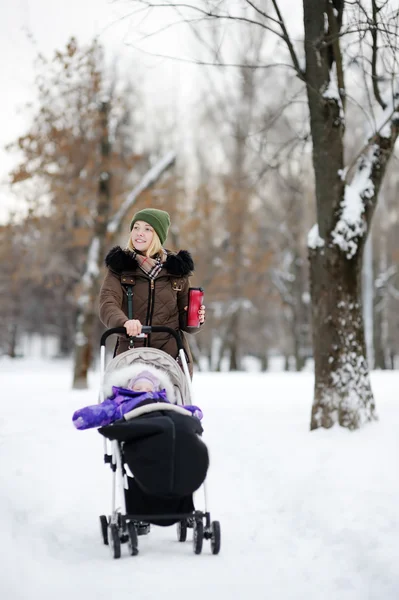 Jeune mère marchant avec bébé en poussette dans le parc d'hiver — Photo