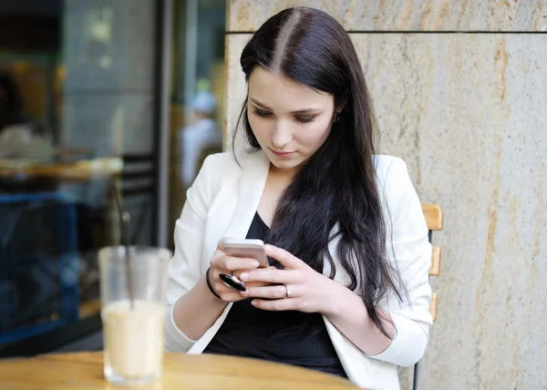 Молодая женщина использует свой мобильный телефон в кафе на открытом воздухе — стоковое фото