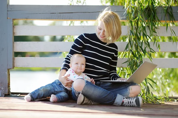 Junge Mutter mit ihrem Baby, das am Laptop arbeitet oder studiert — Stockfoto