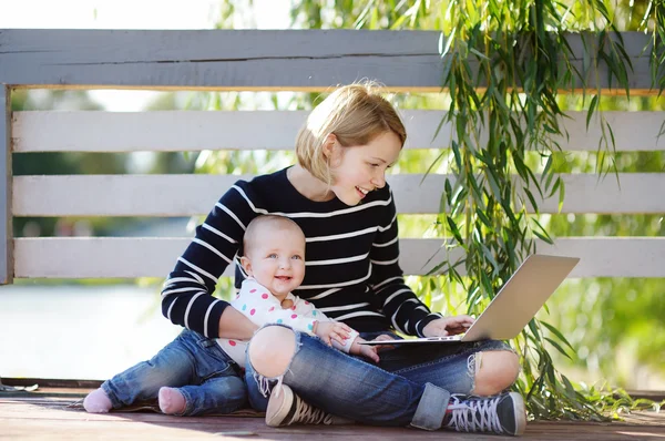 Jovem mãe com seu bebê trabalhando ou estudando no laptop — Fotografia de Stock