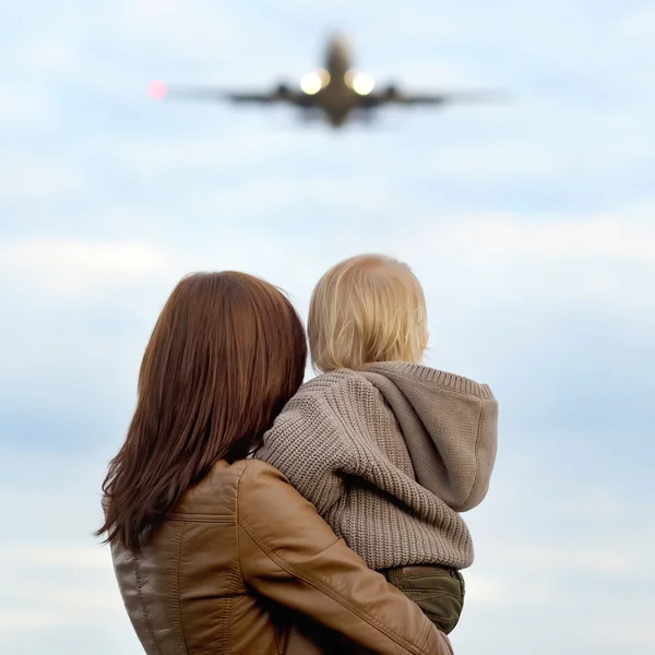 Mujer sosteniendo niño pequeño con avión en el fondo — Foto de Stock