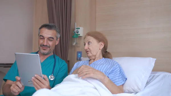 病院のベッドでタブレットで高齢者と話す医師 — ストック写真