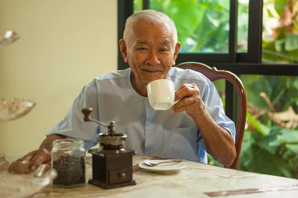 Азиатский пожилой человек со старинной кофемолкой — стоковое фото