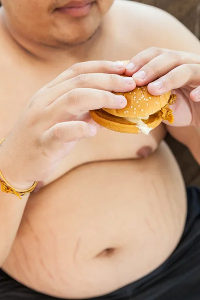 Grasso uomo mangiare hamburger seduto — Foto Stock