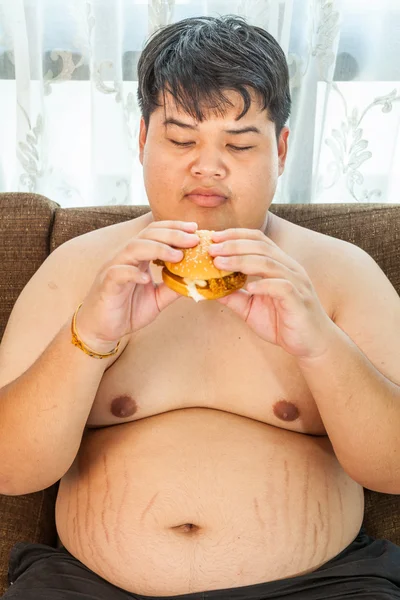 Grasso uomo mangiare hamburger seduto — Foto Stock