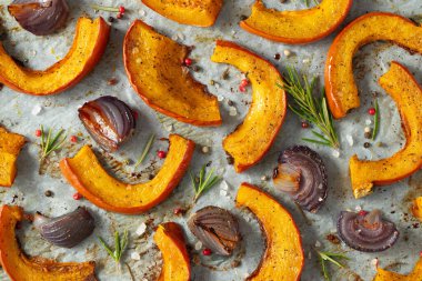 Yakın plan kavrulmuş balkabağı, ilave aromatik otlar, kırmızı soğan, deniz tuzu ve zeytinyağı. Balkabağı sonbahar arkaplanı. Üst görünüm.