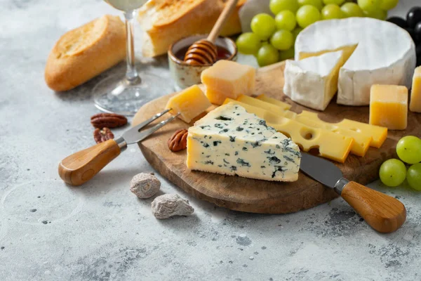 Tasting cheese dish on a wooden plate. Food for wine and romantic date, cheese delicatessen on a light concrete background. with copy space