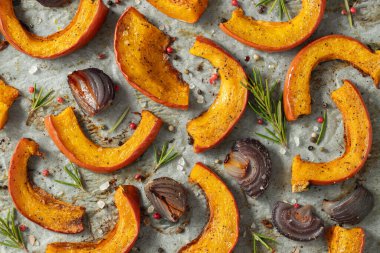 Yakın plan kavrulmuş balkabağı, ilave aromatik otlar, kırmızı soğan, deniz tuzu ve zeytinyağı. Balkabağı sonbahar arkaplanı. Üst görünüm.