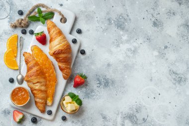 Kahvaltıda tereyağlı ve portakal reçelli taze kruvasan. Beyaz beton bir masada Avrupalı kahvaltısı. Kopyalama alanı olan üst görünüm. Düz yatıyordu