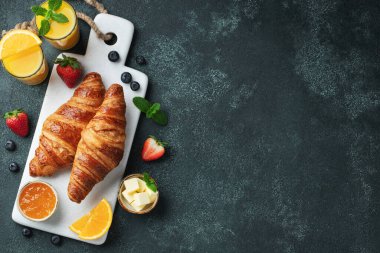 Kahvaltıda tereyağlı ve portakal reçelli taze kruvasan. Siyah beton bir masada Avrupalı kahvaltısı. Kopyalama alanı olan üst görünüm. Düz yatıyordu