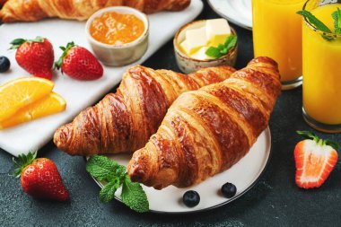 Kahvaltıda tereyağlı ve portakal reçelli taze kruvasan. Koyu beton arka planda Avrupai kahvaltı.