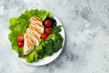 Tavuk göğsü fileto ve domatesli sebze salatası ve açık arkaplanda yeşil yapraklar. Sağlıklı yemek ve keto diyeti kavramı. Kopyalama alanı olan üst görünüm
