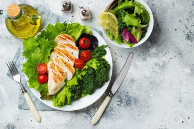 Tavuk göğsü fileto ve domatesli sebze salatası ve açık arkaplanda yeşil yapraklar. Sağlıklı yemek ve keto diyeti kavramı. Kopyalama alanı olan üst görünüm