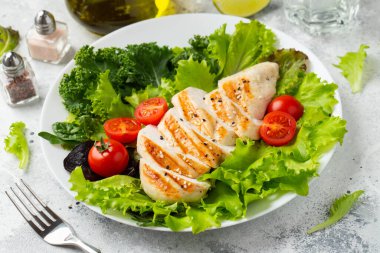 Tavuk göğsü fileto ve domatesli sebze salatası ve açık arkaplanda yeşil yapraklar. Sağlıklı gıda ve keto diyeti kavramı