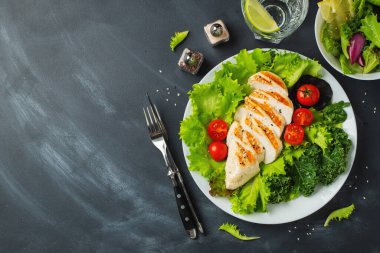 Tavuk göğsü fileto ve domatesli sebze salatası ve siyah arka planda yeşil yapraklar. Sağlıklı yemek ve keto diyeti kavramı. Kopyalama alanı olan üst görünüm