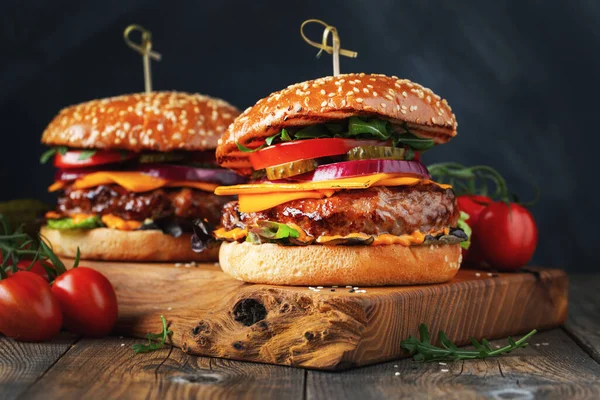 两个美味的自制汉堡包，牛肉，奶酪和蔬菜放在一张古老的木制桌子上。脂肪不健康食品特写 — 图库照片