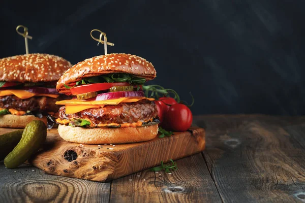 两个美味的自制汉堡包，牛肉，奶酪和蔬菜放在一张古老的木制桌子上。脂肪不健康食品特写。有复制空间 — 图库照片