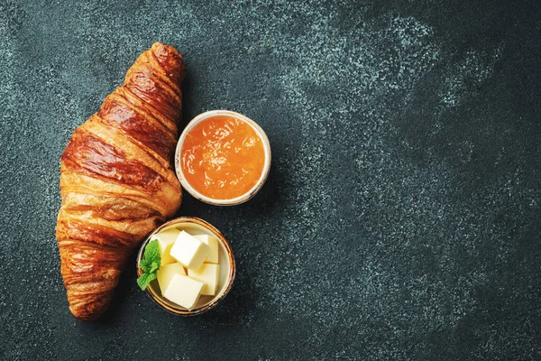 Friss édes croissant vajjal és narancslekvárral reggelire. Kontinentális reggeli egy fekete betonasztalon. Felülnézet fénymásoló felülettel. Lapos fektetés — Stock Fotó