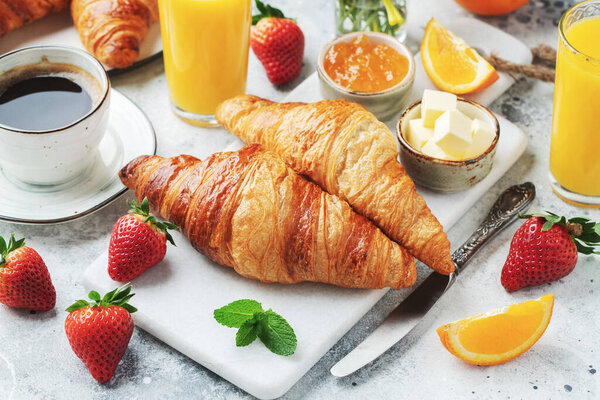 Fresh sweet croissants with butter and orange jam for breakfast. Continental breakfast on a white concrete table.