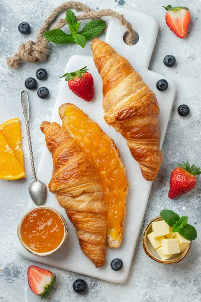 Färska söta croissanter med smör och apelsinsylt till frukost. Kontinental frukost på ett vitt betongbord. Högst upp. Platt äggläggning — Stockfoto