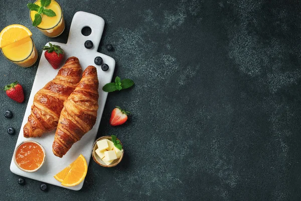 Friss édes croissant vajjal és narancslekvárral reggelire. Kontinentális reggeli egy fekete betonasztalon. Felülnézet fénymásoló felülettel. Lapos fektetés — Stock Fotó