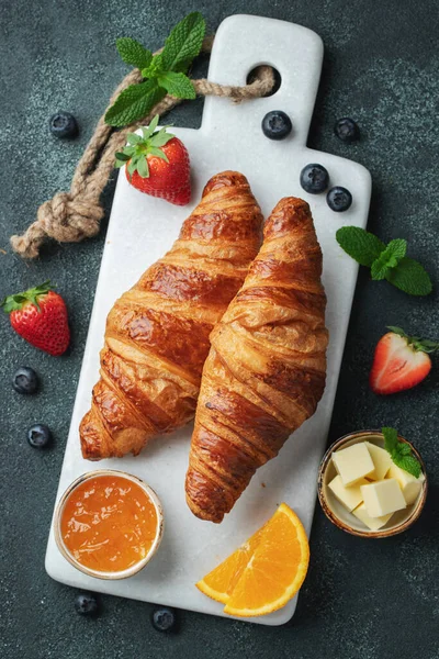 Friss édes croissant vajjal és narancslekvárral reggelire. Kontinentális reggeli egy fekete betonasztalon. Első látásra. Lapos fektetés — Stock Fotó