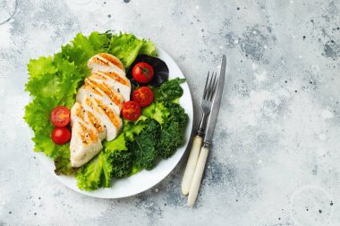Tavuk göğsü fileto ve domatesli sebze salatası ve açık arkaplanda yeşil yapraklar. Sağlıklı yemek ve keto diyeti kavramı. Kopyalama alanı olan üst görünüm