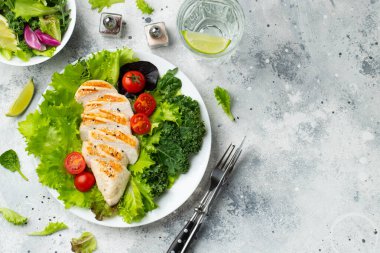 Tavuk göğsü fileto ve domatesli sebze salatası ve açık arkaplanda yeşil yapraklar. Sağlıklı yemek ve keto diyeti kavramı. Kopyalama alanı olan üst görünüm