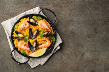 Geleneksel İspanyol deniz ürünleri paella tavada nohut, karides, midye, kahverengi beton arka planda mürekkep balığı. Kopyalama alanı olan üst görünüm