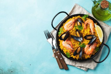 Geleneksel İspanyol deniz ürünleri paella tavada nohut, karides, midye, açık mavi beton arka planda mürekkep balığı. Kopyalama alanı olan üst görünüm