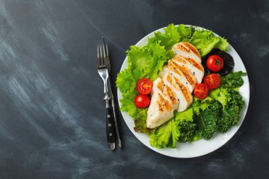 Tavuk göğsü fileto ve domatesli sebze salatası ve siyah arka planda yeşil yapraklar. Sağlıklı yemek ve keto diyeti kavramı. Kopyalama alanı olan üst görünüm.