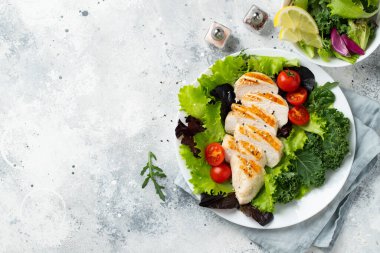 Tavuk göğsü fileto ve domatesli sebze salatası ve açık arkaplanda yeşil yapraklar. Sağlıklı yemek ve keto diyeti kavramı. Kopyalama alanı olan üst görünüm