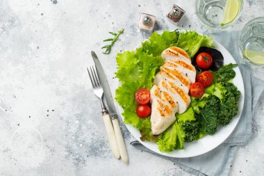 Tavuk göğsü fileto ve domatesli sebze salatası ve açık arkaplanda yeşil yapraklar. Sağlıklı yemek ve keto diyeti kavramı. Kopyalama alanı olan üst görünüm.