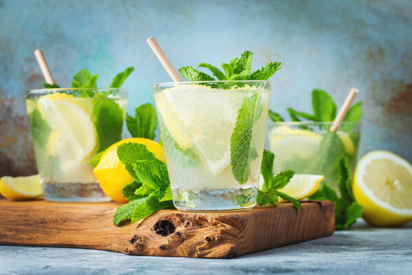 Two glass with lemonade or mojito cocktail with lemon and mint, cold refreshing drink or beverage with ice on rustic blue background