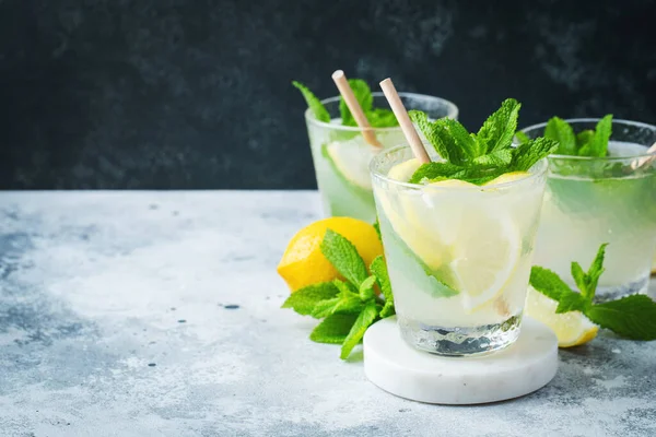 Two glass with lemonade or mojito cocktail with lemon and mint, cold refreshing drink or beverage with ice on rustic blue background. Copy space — Stock Photo, Image