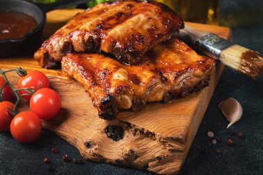 Baharatlı, ızgara pirzola. Barbekü, acı biber ve taze domatesle servis edilir. Eski bir ahşap kesim tahtasının üzerinde.