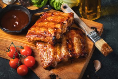 Baharatlı, ızgara pirzola. Barbekü, acı biber ve taze domatesle servis edilir. Eski bir ahşap kesim tahtasının üzerinde.