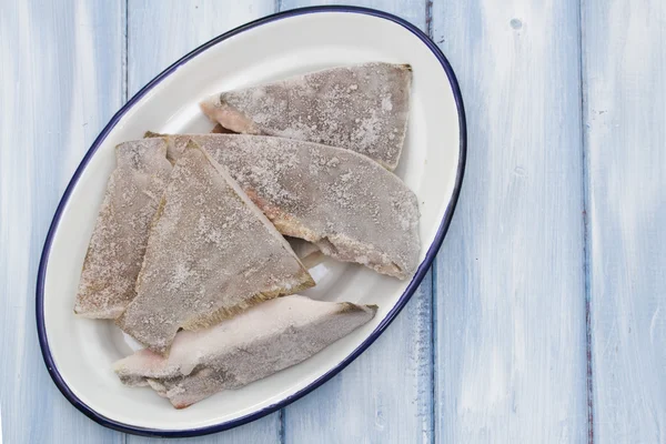 Pescado congelado en plato blanco en fondo azul de madera —  Fotos de Stock