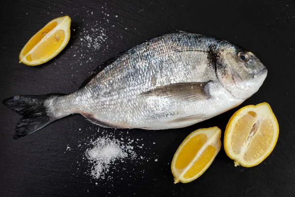 Fresh fish wth lemon and salt on black ceramic — Stock Photo, Image