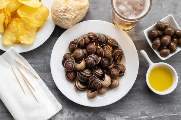 Boiled snails with bear, bread, olives and potato chips on blue — Stock Photo, Image