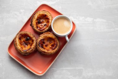 Tipik Portekiz yumurtalı tart pastel de nata ve turuncu tabakta bir fincan kahve.