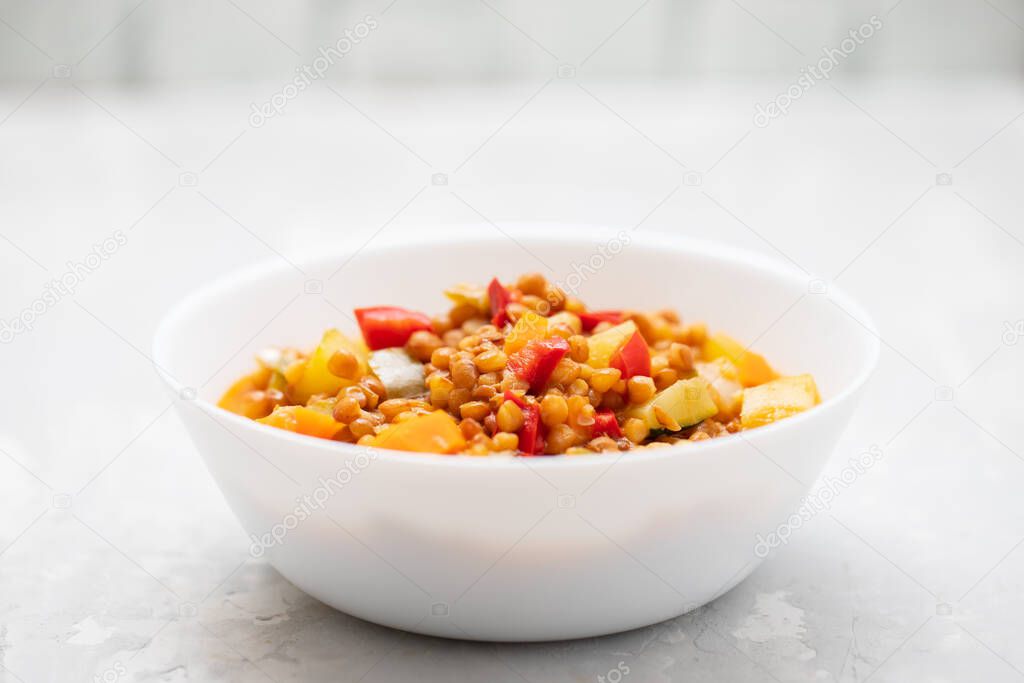 lentil with pepper, courgette and onion on white dish on ceramic background