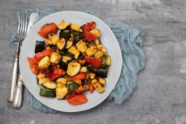 Fırında kabak ve domates tabakta çatal ve seramik zemin üzerinde bıçak.