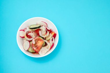 Beyaz kasede mavi kağıtta taze sebze salatası.