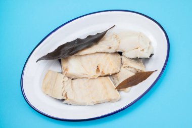 Haşlanmış morina balığı ve defne yaprağı mavi arka planda beyaz tabak.