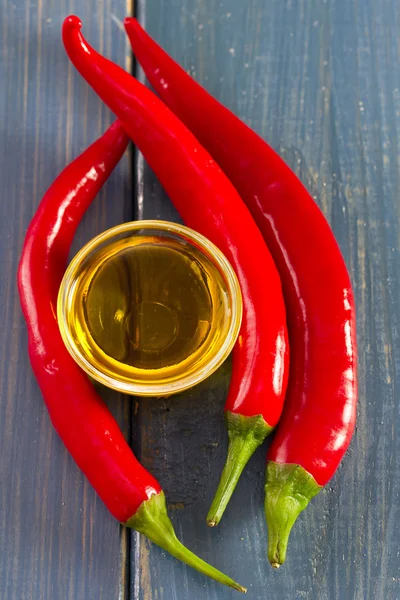 Oil and red pepper on blue wooden background — Stock Photo, Image